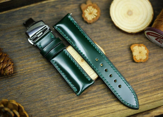 Army green Shell Cordovan leather watch strap with deployant clasp on rustic wooden background - premium horsehide watch band